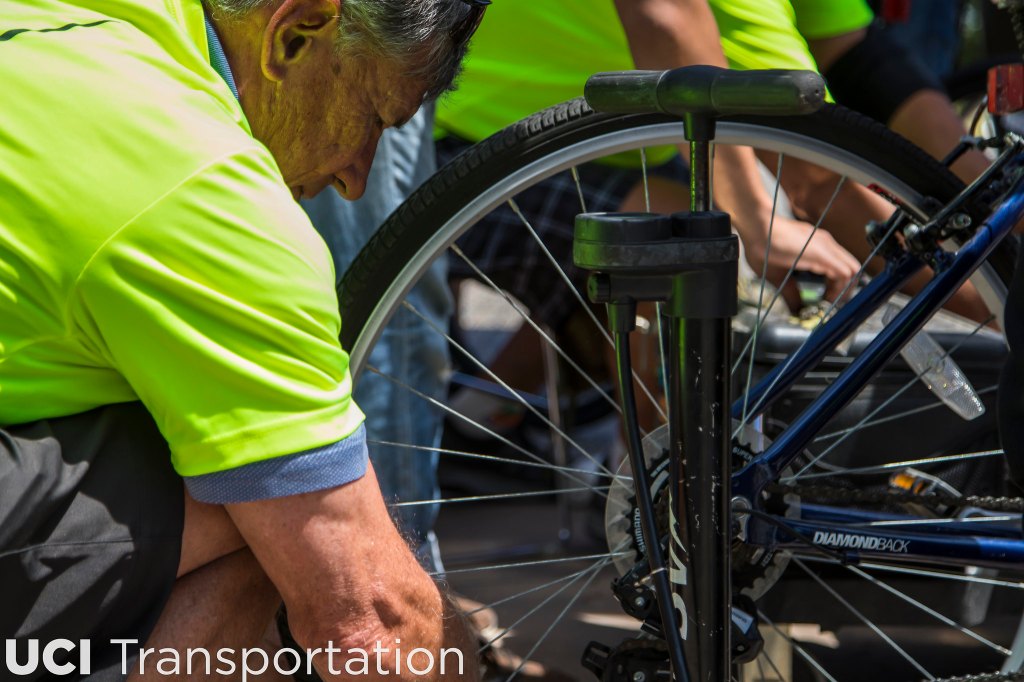 An older man in a hi-vis T-shirt pumping up the rear tyre on someone's bicycle