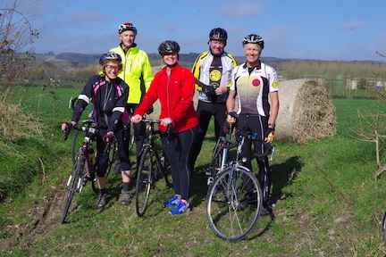 A group of 5 cyclists with bicycles out on a ride on a sunny day standing in a field. A group of 5 cyclists with bicycles out on a ride on a sunny day standing in a field.