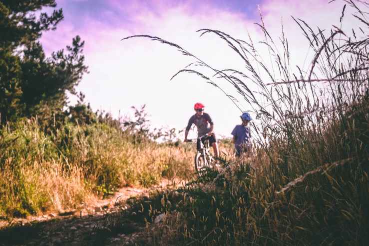 Two adults riding towards the viewer in the evening sun along a flatish offroad route.