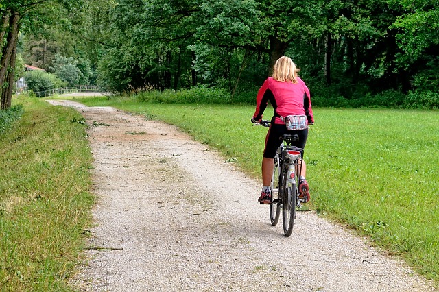 A woman cycling into the greenery on a quiet non-tarmaced road on a dry day.