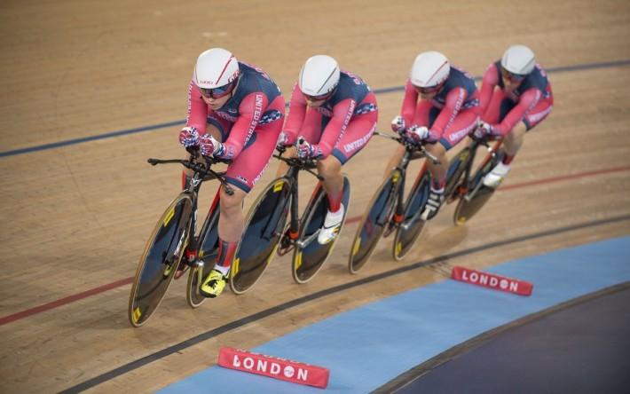 Four women track cyclists racing around the track in pink and grey kit