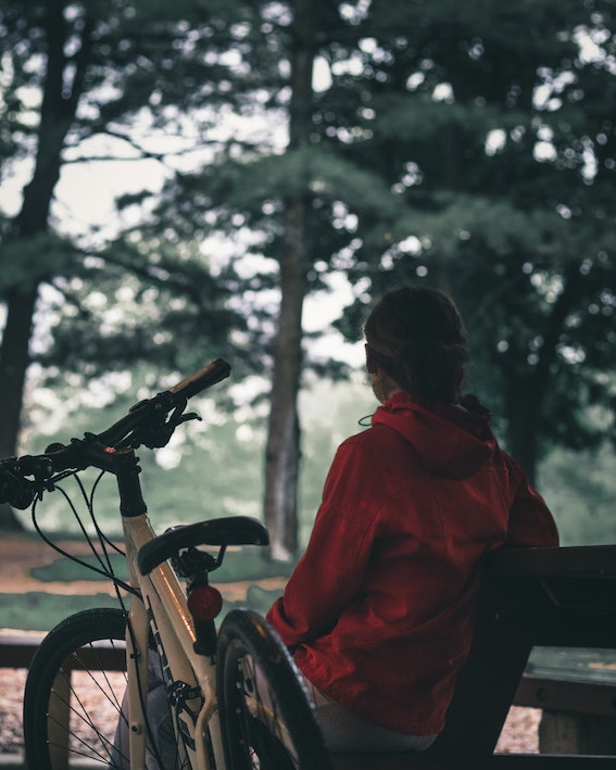 Woman sitting on bench under trees next to her cycle