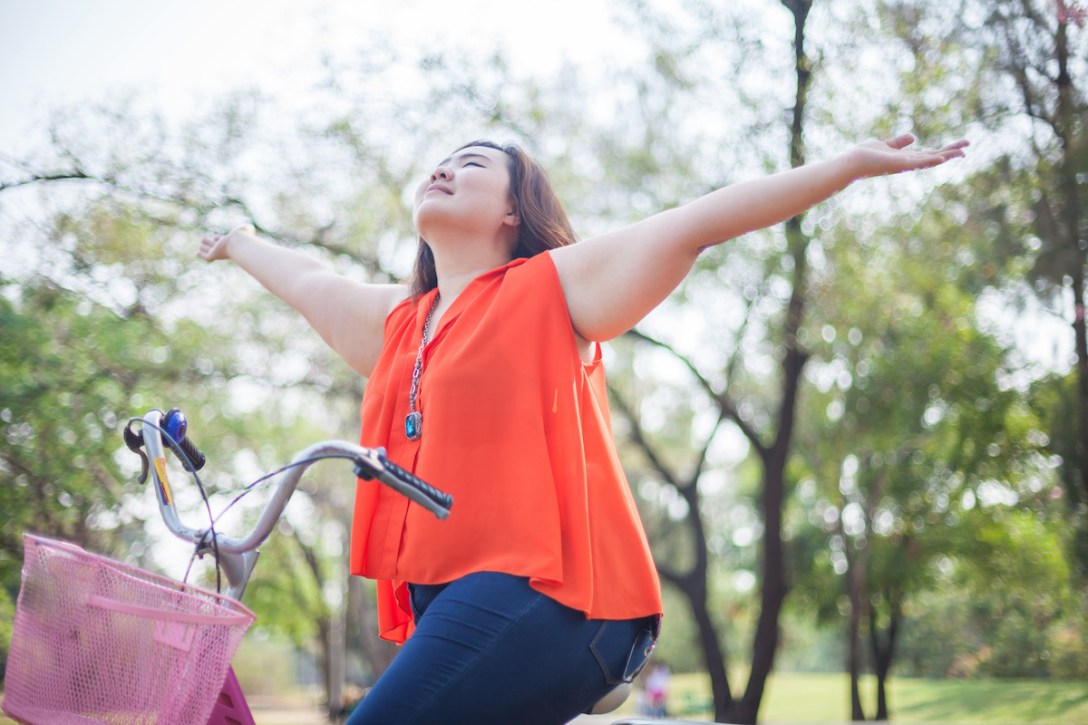 Asian woman outstretched with bicycle outdoor in a park